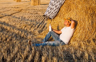 saman haystacks ve süt içecek hasat sonrası dinlenme bir hasır şapka giyen adam