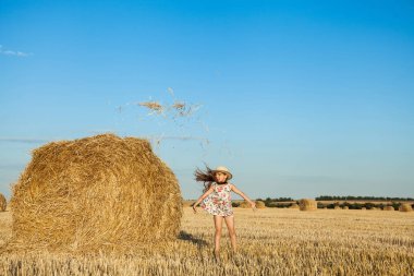 Sevimli kız hasır şapka giyen atlama ve saman buğday alanında kadar sıcak ve güneşli yaz akşamı atma.