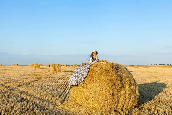 Sevimli kız bir haystack köyü hasır şapka giyiyor süt içip pişmiş mal buğday alanında sıcak ve güneşli yaz akşamı. Sevimli küçük çocuk çavdar alanında günbatımı.