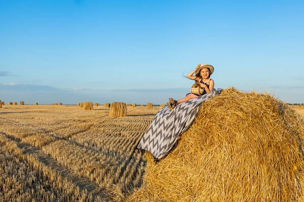 Sevimli kız bir haystack köyü hasır şapka giyiyor süt içip pişmiş mal buğday alanında sıcak ve güneşli yaz akşamı. Sevimli küçük çocuk çavdar alanında günbatımı.