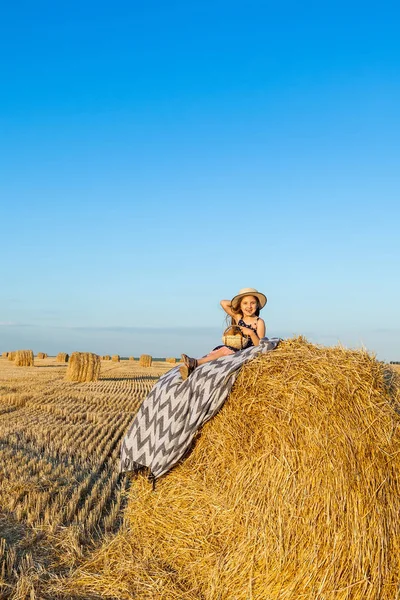 Sevimli kız bir haystack köyü hasır şapka giyiyor süt içip pişmiş mal buğday alanında sıcak ve güneşli yaz akşamı. Sevimli küçük çocuk çavdar alanında günbatımı.