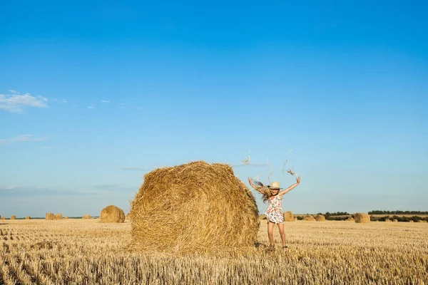 Sevimli kız hasır şapka giyen atlama ve saman buğday alanında kadar sıcak ve güneşli yaz akşamı atma.