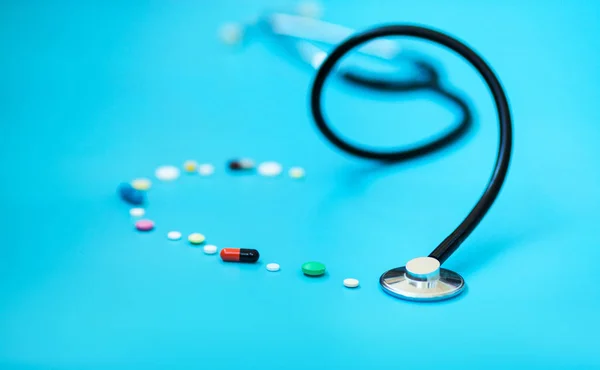 医学概念 药物听诊器和不同的胶囊和药丸形成的心脏在蓝色背景的形状 保健或疾病 医院或药房的片剂或药物 — 图库照片