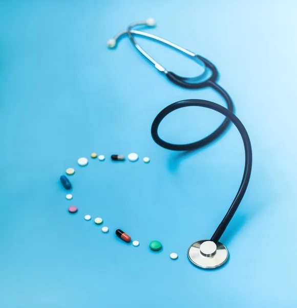 医学概念 药物听诊器和不同的胶囊和药丸形成的心脏在蓝色背景的形状 保健或疾病 医院或药房的片剂或药物 — 图库照片