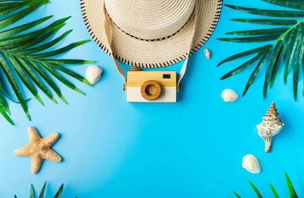 Traveler accessories, wooden camera and tropical palm leaf branches on blue background with empty space for text. Travel vacation concept. Summer background. Flat lay, top view.