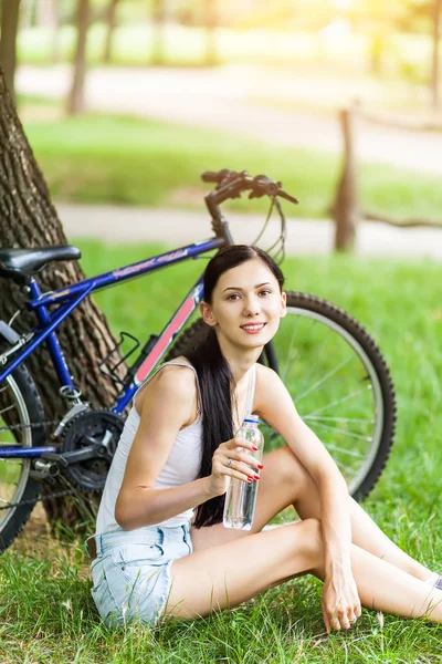 Şehir Parkı içme suyu çimenlerin üzerinde rahatlatıcı Bisiklet ile güzel bir kız. Aktif insanlar. Açık havada