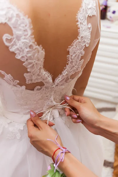 Wedding concept. A close-up of the bride\'s back in a tender wedding lace dress. The process of fastening the dress.