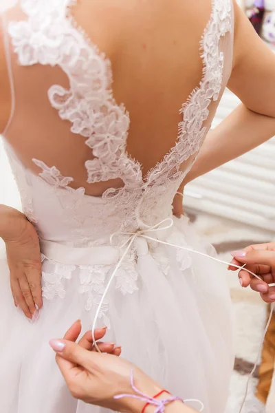 Wedding concept. A close-up of the bride\'s back in a tender wedding lace dress. The process of fastening the dress.