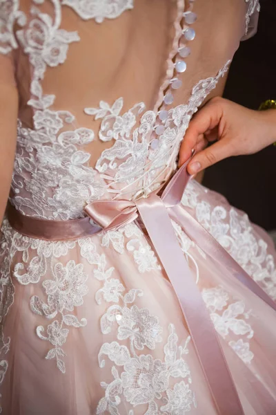 Wedding concept. A close-up of the bride\'s back in a tender wedding lace dress. The process of fastening the dress.