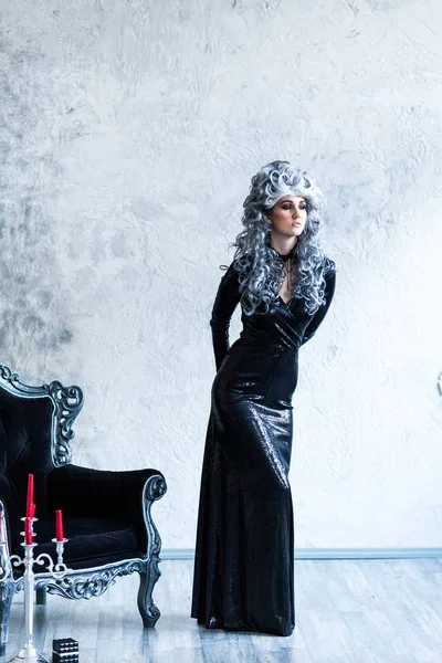 Halloween. Portrait of a gorgeous young glamour beautiful woman vampire baroque aristocrat witch in black dress with gray curly hair in the ancient castle.
