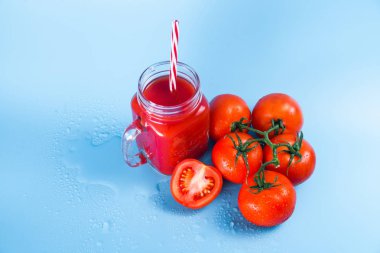 Mason kavanoza ve taze üzüm domates ve bütün mavi ıslak zemin üzerine yarım domates domates suyu