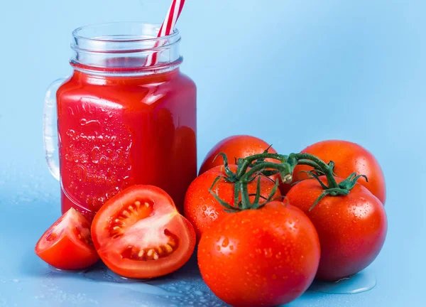 Mason kavanoza ve taze üzüm domates ve bütün mavi ıslak zemin üzerine yarım domates domates suyu