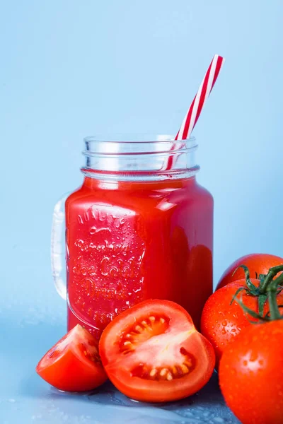 Mason kavanoza ve taze üzüm domates ve bütün mavi ıslak zemin üzerine yarım domates domates suyu