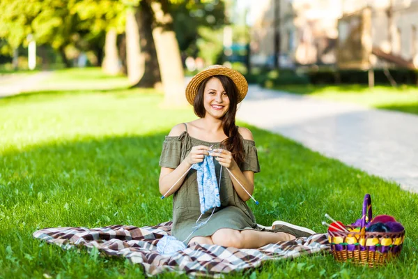 市公園緑の草の上に座っていると 夏の日の編み針と青いセーターを編む若い女性 どこでもクリエイティブを取得します — ストック写真