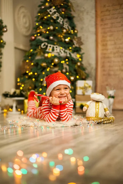 Cute Little Boy Striped Red Pajamas Hat Lies Christmas Tree — Stock Photo, Image