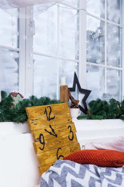 Vintage Christmas interior with Christmas decoration against Snowy winter window, cozy bedroom, with a blanket and a panel with a clock pattern