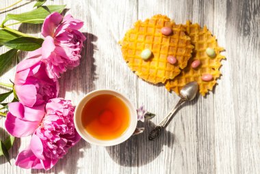 Fincan yeşil çay ve bahar peonies çiçeği waffle ve karamel eski bir ahşap zemin üzerine. Rustik.