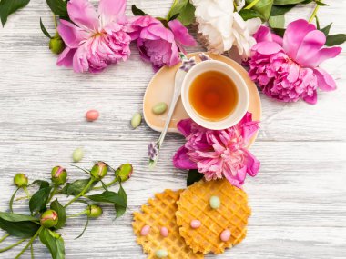 Fincan yeşil çay ve bahar peonies çiçeği waffle ve karamel eski bir ahşap zemin üzerine. Rustik.