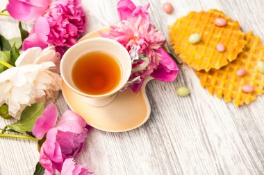 Fincan yeşil çay ve bahar peonies çiçeği waffle ve karamel eski bir ahşap zemin üzerine. Rustik.