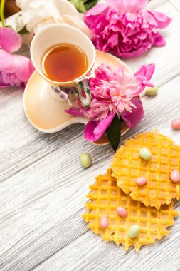 Fincan yeşil çay ve bahar peonies çiçeği waffle ve karamel eski bir ahşap zemin üzerine. Rustik.