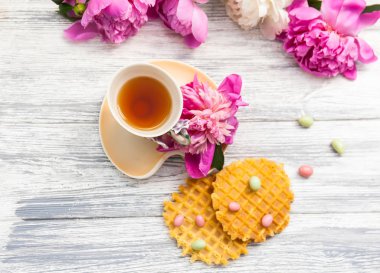 Fincan yeşil çay ve bahar peonies çiçeği waffle ve karamel eski bir ahşap zemin üzerine. Rustik.
