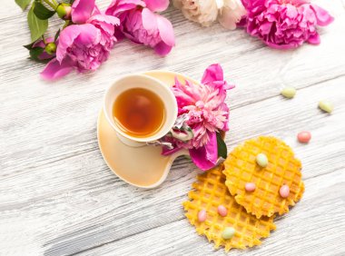 Fincan yeşil çay ve bahar peonies çiçeği waffle ve karamel eski bir ahşap zemin üzerine. Rustik.