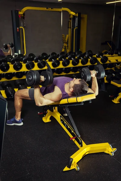 Erkek sporcu spor salonunda halterlerle ağırlık kaldırıyor.