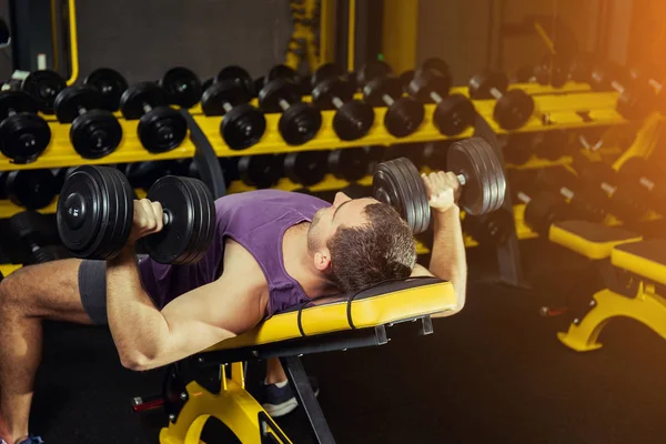 Erkek sporcu spor salonunda halterlerle ağırlık kaldırıyor.