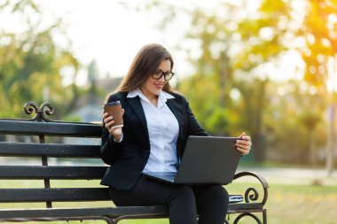 Kahve molası. Parkta bir bankta oturan iş kadını ile bir dizüstü bilgisayar çalışma
