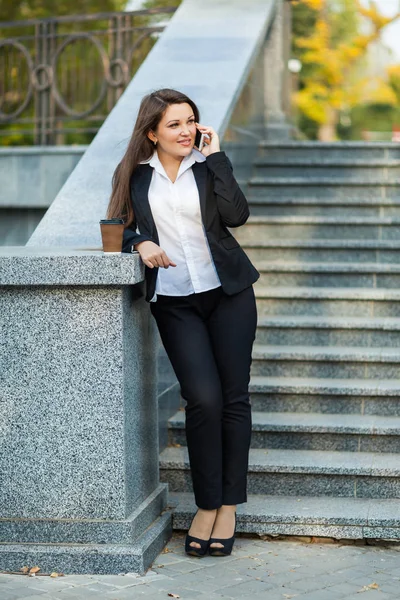 Successful businesswoman with coffee talking on cellphone while walking outdoor. City business woman working.