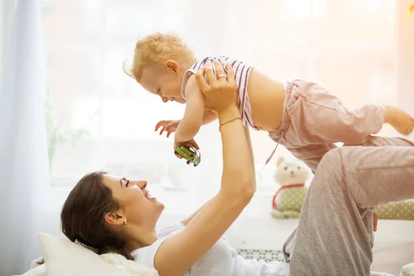 Ung mamma kysser hennes baby som ligger på sängen — Stockfoto