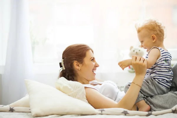 Ung mamma kysser hennes baby som ligger på sängen — Stockfoto