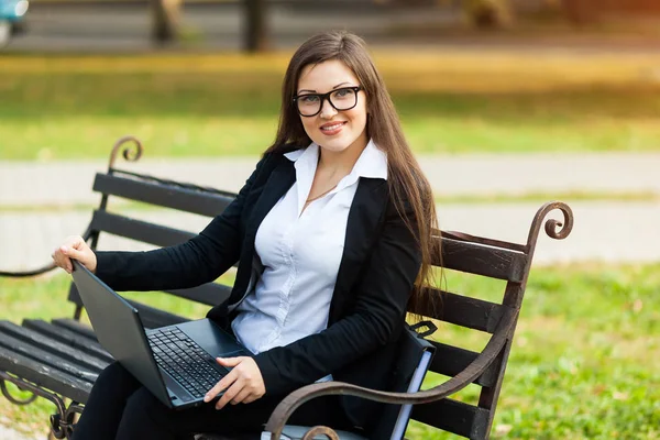 坐在公园里的商务女性坐在长椅上，用笔记本电脑工作 — 图库照片
