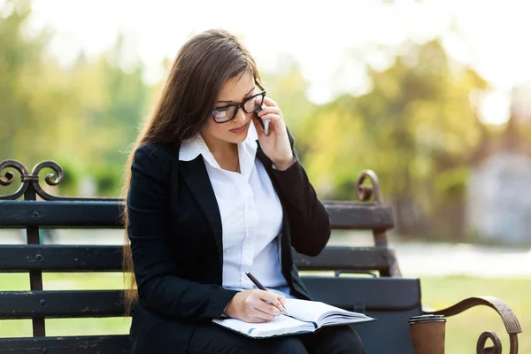Empresária feliz chamando no telefone celular e tomar notas ao ar livre — Fotografia de Stock