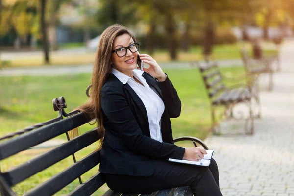 Happy businesswoman calling on mobile phone and taking notes outdoor — Stock Photo, Image