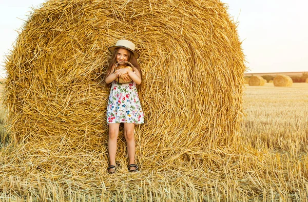 Menina adorável no campo de centeio no pôr do sol com uma cesta de pão . — Fotografia de Stock