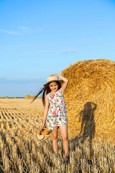 Menina adorável no campo de centeio no pôr do sol com uma cesta de pão . — Fotografia de Stock