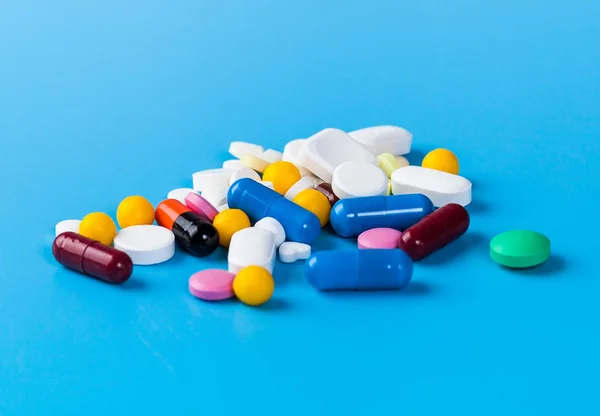 Pastillas, tabletas y cápsulas medicinales sobre fondo azul — Foto de Stock