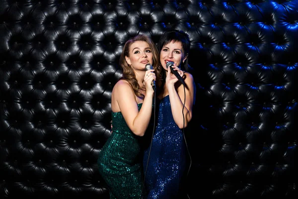 Meninas cantando bonitas com música de karaoke microfone no palco no fundo escuro — Fotografia de Stock