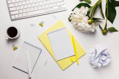 Ev konseptinde çalışmak. Üzerinde mikroyeşil sandviç, not defteri, klavye, beyaz ve sarı kalem, buruşmuş kağıt top, bir buket piyon ve kahve fincanı olan beyaz masa.