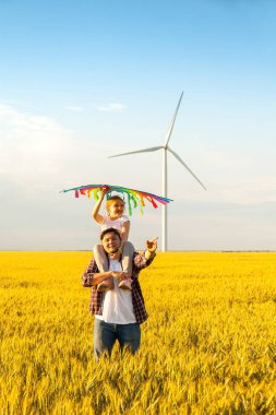 Mutlu baba kızını sırtında taşıyor, eğleniyor, yazın doğada uçurtmayla çayırda oynuyor.