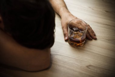 Bunalımlı bir adam, sarhoş, elinde bir bardak viski, yoksulluk, alkolizm ve depresyon konseptiyle masada uyuyor.