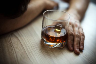 Depresyondaki adamın ellerini kapat, elinde bir bardak viskiyle masanın üstünde uyu. Yoksulluk, alkolizm ve depresyon kavramı. Yumuşak odak