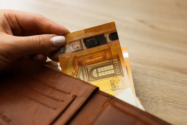 Hand holding Euro banknote in Wallet stuffed on the wooden table. Stuffed Leather Wallet. Euro Bills in Wallet.