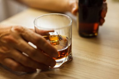 Viski ya da konyak bardağı, buz ve şişeyle ahşap arka planda bir el. Yoksulluk, alkolizm ve depresyon kavramı