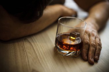 Depresyondaki adamın ellerini kapat, elinde bir bardak viskiyle masanın üstünde uyu. Yoksulluk, alkolizm ve depresyon kavramı