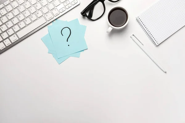 İş planı. İş yeri, yazılı yapışkan not soru işareti, kalem, bardak, kahve, not defteri ve klavye beyaz masa üzerinde fotokopi alanı ile çalışıyor.