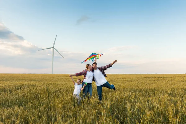 Happy family having fun with kite on the field. Beautiful family with flying colorful kite over clear sky. Free, freedom concept.