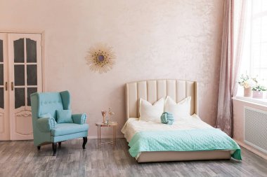 Pembe, mavi ve altın rengi yatak odasının gerçek fotoğrafı, büyük bir pencere, eski kapılar, bej bir yatak, mavi rahat bir koltuk, altın aynalı bir kahve masası.