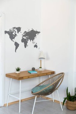 Scandi tarzında beyaz ve ahşap parlak çalışma alanı. Lambalı ve defterli şık bir masa, modern rattan sandalye, beyaz bir duvarda dünya haritası.
